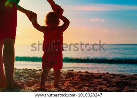 Silhouette of father and little daughter on beach