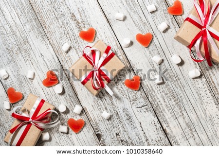 Valentines Day candy hearts marshmallows and box of gifts in craft paper over white wooden background.