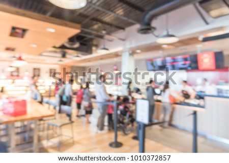 Blurred family members with stroller queuing behind stanchion barriers check-out counter at bakery in Texas, USA. Large wall mount led menu board digital signage. Abstract background crowd waiting