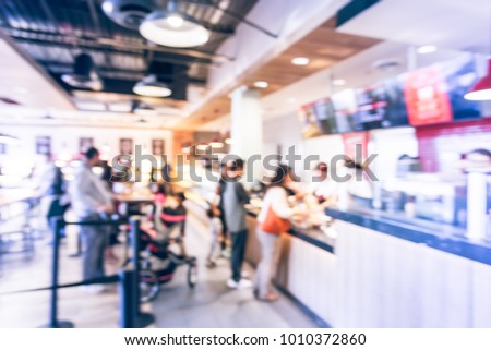 Blurred family members with stroller queuing behind stanchion barriers check-out counter at bakery in Texas, USA. Big wall mount led menu board digital signage. Abstract crowd waiting. Vintage tone