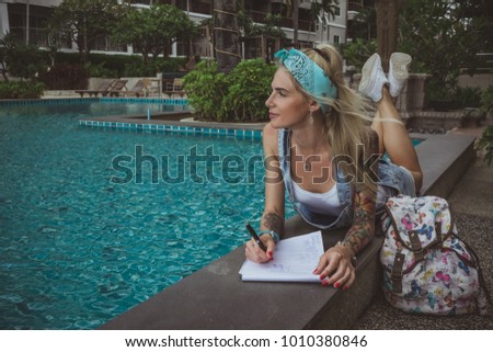 A beautiful college student at the pool performs homework. Dreamy image of a modern girl. Model of tattoo.
