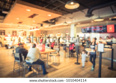 Blur modern hipster open coffee shop, self-serve bakeries in USA. Long people sit and stand queuing behind stanchion barriers check-out counter. Wall mount led menu board digital signage. Vintage tone