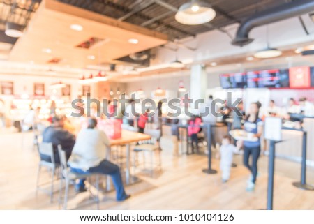 Blurred modern hipster open coffee shops, self-serve bakeries in USA. Long people sit and stand queuing behind stanchion barriers check-out counter. Large wall mount led menu board digital signage.