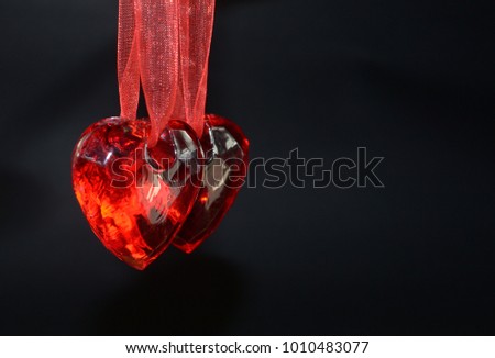 Two red glass hearts are hanging on red ribbon
