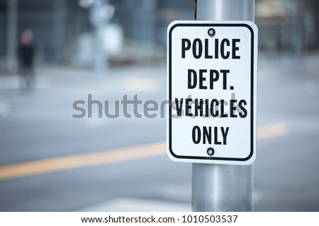 Close up on a Police Department Vehicles Only parking sign, on a metal light post, with a blurry city background
