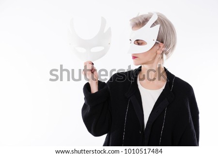 Young beautiful blonde woman in the white mask, holding a mask. Isolated on white background. Bipolar portrait