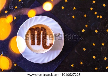 white cup of coffee with the symbol of the zodiac scorpion on milk foam