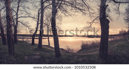Vintage landscape witn sunset over lake. Trees on coast, clouds reflection in water, panorama