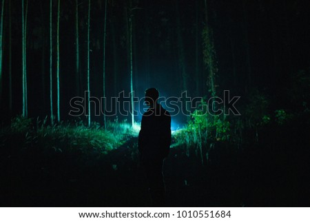 Lonely man silhouette with lantern in the dark scary forest during hazy weather
