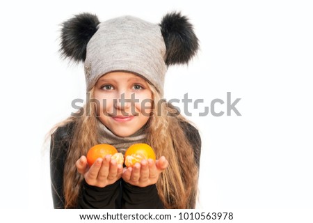 Young girl in a warm hat holds a tangerine in her hands and smiles on a white background. She is a vegan. Place for text