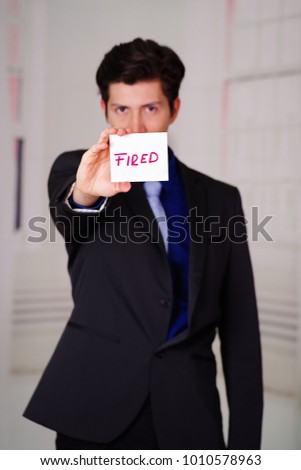 Sad business man holding a paper of fired text on it in his hand, in a blurred background