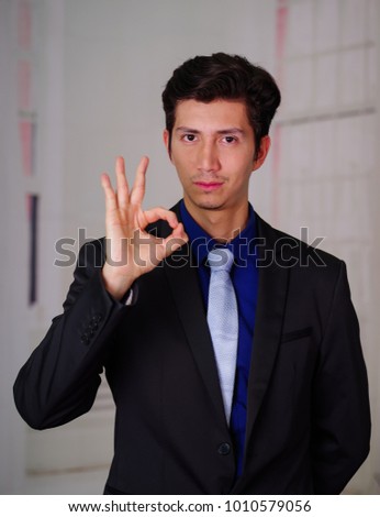 Close up of businessman wearing a suit, doing a sign of ok with his hand, in a blurred background