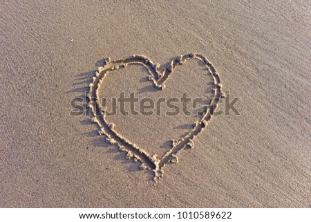 Drawing heart shape on the sand of the beach in the middle with a little shadow, feeling love, free space for text. Concept Valentine's day or Wedding invitation.
