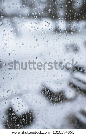 Raindrops on window with blurred garden in snow on background.