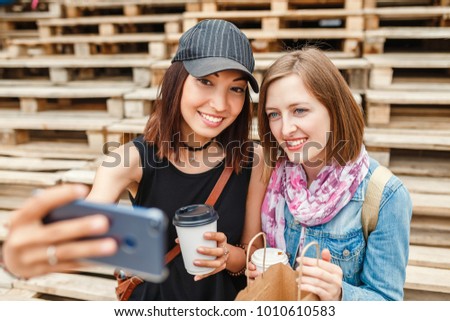 Outdoor portrait of two young students and friends taking selfie photos with a smartphone