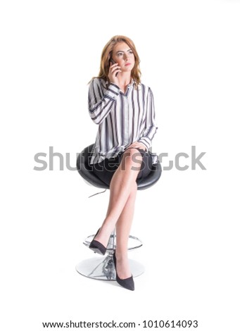 Young woman sitting on a tall seat, with a mobile phone to her ear, isolated on a white background. Royalty-Free Stock Photo #1010614093