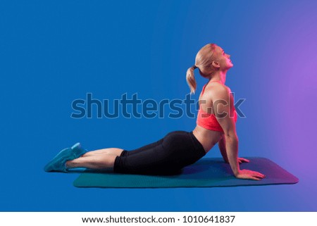 blond girl is engaged in stretching on a blue yoga mat on a blue background. Space for text