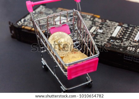 Stack of coins bitcoin in mini shopping cart toy on the video card, concept of mining. Electronic virtual money for web banking and international network payment. Symbol of crypto currency