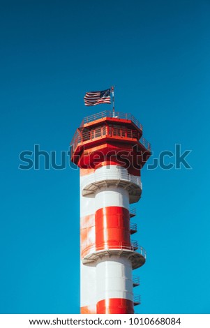 Lighthouse in Oahu, Hawaii. American flag on the top, waving in the wind. Bright blue sunny sky. 