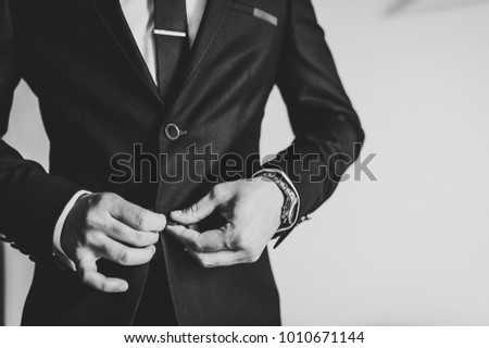 Man fastens the buttons. The groom in a suit, shirt, tie is standing on white background. Close up. Black and white photo.