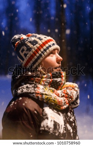 Portrait of woman looking up in knitted cap at evening winter forest on blurred background