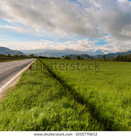 Highway in Piedmont on the background of snow capped Italian Alps. View of the mountain valley with asphalt road at sunrise 