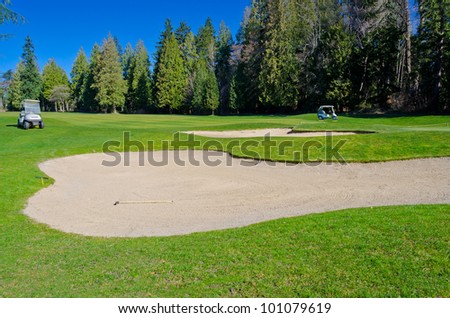 Sand bunker on the golf course with the golf carts at the back.