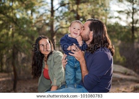 Father kissing baby boy, mother sitting in the background. Shallow DOF, focus on baby.