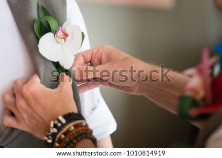 Close-up picture of groomsman putting flower brooch on groom's vest