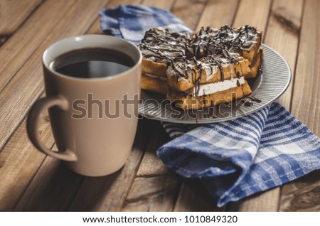 waffles with cream and chocolate on the plate and coffee on a wooden table. 