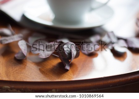 Cup of coffee staying on a wooden table. Floral element as decoration. Morning light, everything ready for breakfast. 
