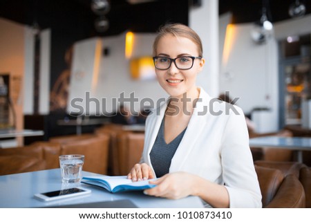young smiling business woman in glasses with diary in hands in cafe