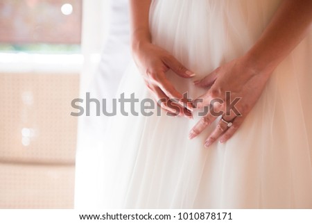 Bright Close-up picture on bride’s hands with engagement rings resting on wedding dress 