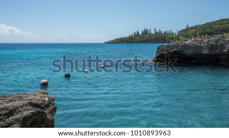 Stunning Tadine Bay with turquoise Pacific Ocean waters, lush greenery, rock and buoys on the coast of Mare, New Caledonia Royalty-Free Stock Photo #1010893963