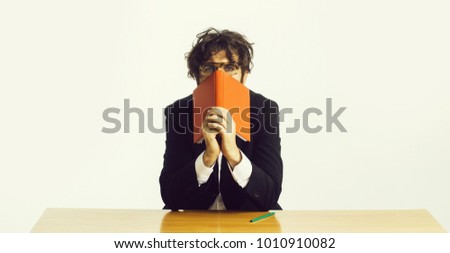 young handsome bearded crazy emotional man scientist or professor with long beard and teacher glasses with pencil and red book or notepaper sitting at table isolated on white background