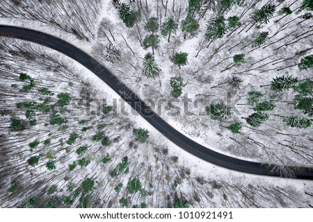 Aerial view of winter road in snowy forest. Drone captured shot from above. Royalty-Free Stock Photo #1010921491