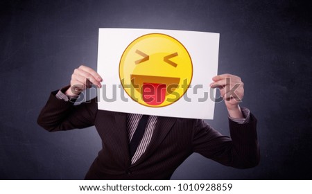 Young businessman hiding behind a playful emoticon on cardboard 