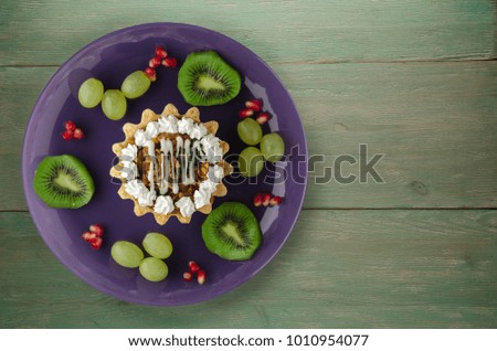 dessert of cake and fruit (grapes, kiwi, pomegranate) on a wooden background. dessert on a plate top view