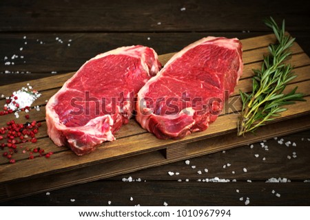 fresh raw new-york steak on wooden Board on wooden background with salt and pepper in a rustic style, top view Royalty-Free Stock Photo #1010967994