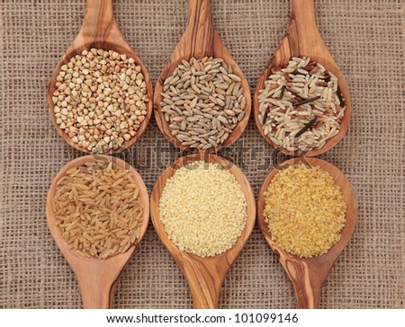 Cereal and grain selection of bulgur wheat, buckwheat, couscous, rye grain and brown and wild rice in olive wood spoons on hessian sacking background. Royalty-Free Stock Photo #101099146