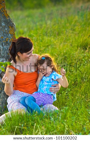 mother, daughter, woman and child sitting in grass near a tree a family photo on their faces joy and emotion