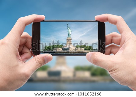 Traveler holding smartphone to take a photo of The Statue of Liberty, Landmarks of New York City, USA
