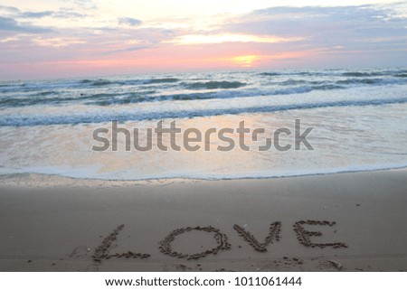 valentine day concept - hand written LOVE text on sand with sea and sunrise background.