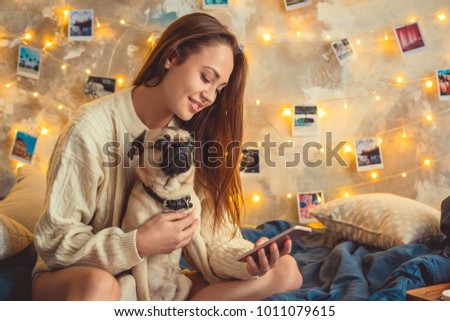 Young woman weekend at home decorated bedroom with dog using smartphone