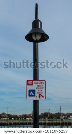 A lamp post at a local marina has a sign posted that reads, No Parking except vehicles with permit, for handicapped boaters to park.