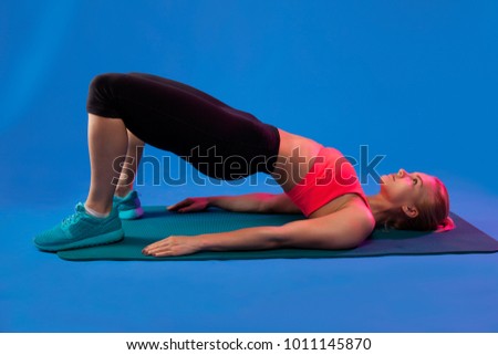 blond girl is engaged in stretching on a blue yoga mat on a blue background.