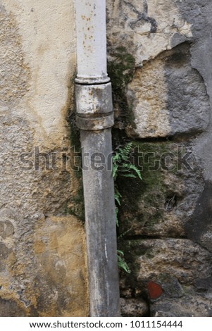 Close up view of an old rusty gutter fixed to an ancient stone wall. Join of two tubes visible. Vertical position. Weathered and aged elements. Beige, grey and brown colors. Abstract urban picture. 