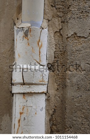 Close up view of an old rusty gutter fixed to an ancient stone wall. Join of two tubes visible. Vertical position. Weathered and aged elements. Beige, grey and brown colors. Abstract urban picture. 