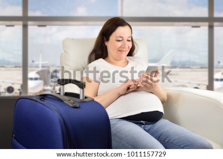 Pregnant woman texting with a smart phone and waiting for her flight in a VIP area and VIP zone aiport