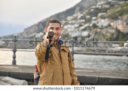 Tourist boy holding a action camera in his hands by the sea